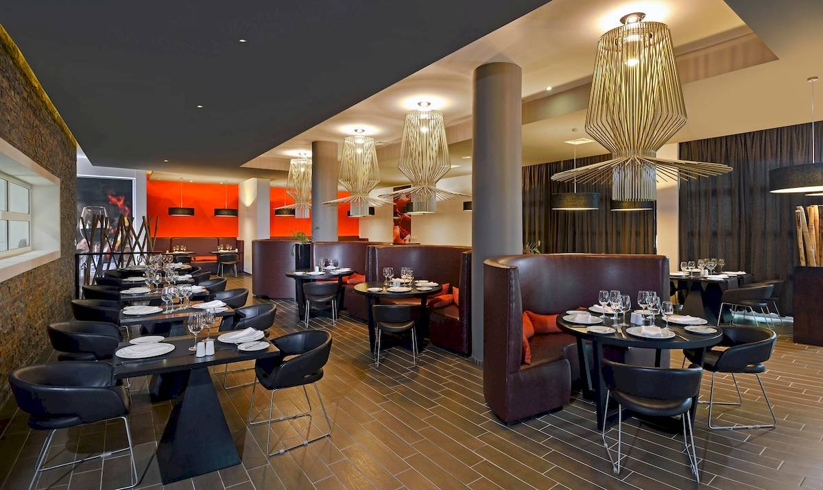 Innenansicht eines modernen Hotelrestaurants mit dunklen Möbeln und großen Leuchten.