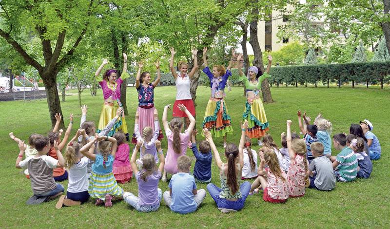 Kinder sitzen auf dem Rasen und beobachten ein Animationsteam im Park.