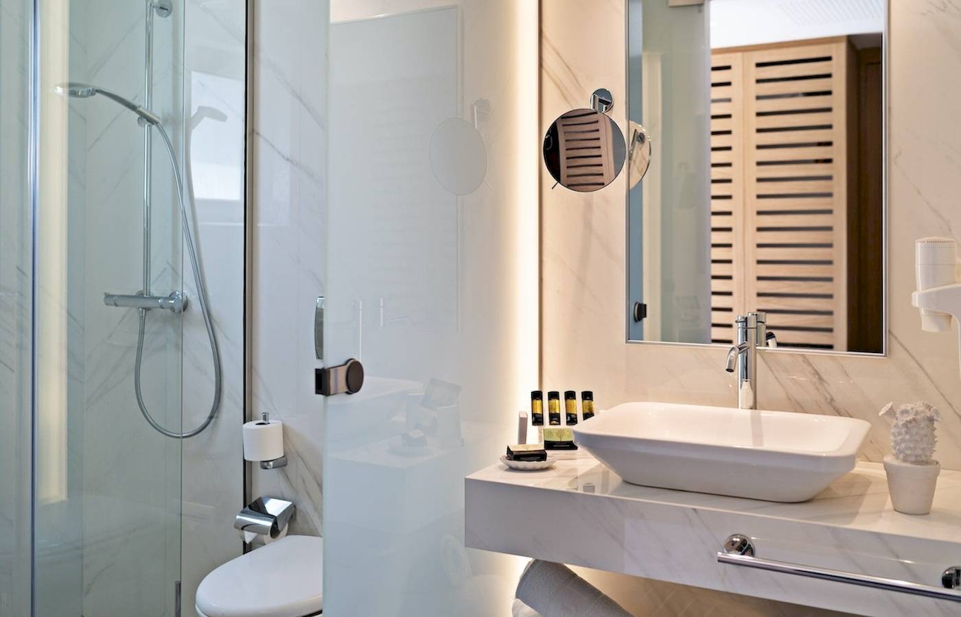 Innenansicht eines Badezimmers im Pilot Beach Resort mit einer Glasdusche, einem Waschbecken, einem Spiegel und einer Toilette.