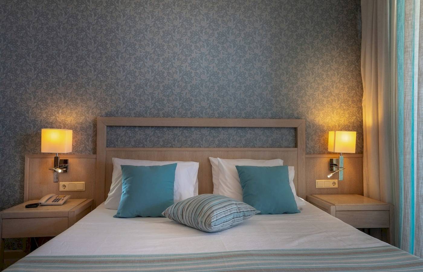 Doppelbett im Pilot Beach Resort Zimmer mit blauen Kissen und weißen Laken.