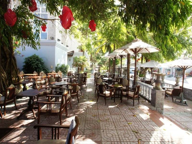Außenbereich des Novela Muine Resort & Spa mit Tischen und Stühlen unter Schirmen
