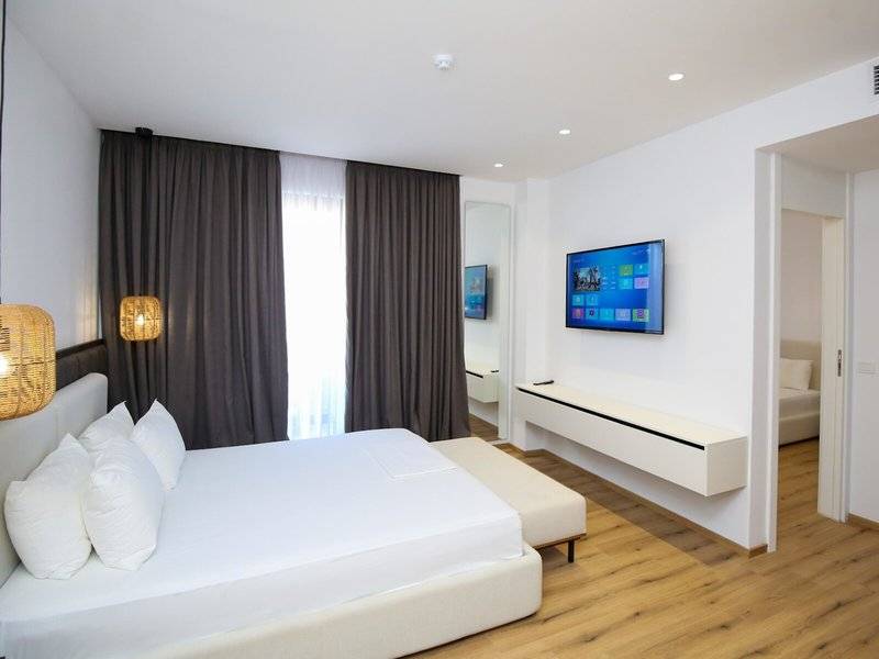 Hotelzimmer im Oricon Coast Luxury Resort mit einem großen Bett, weißen Kissen, einem Fernseher an der Wand und einem Fenster mit Vorhängen.