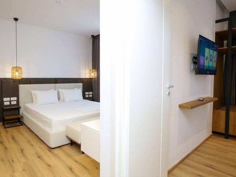 Innenansicht eines eleganten Hotelzimmers mit Doppelbett, Flachbildfernseher an der Wand und Holzboden.