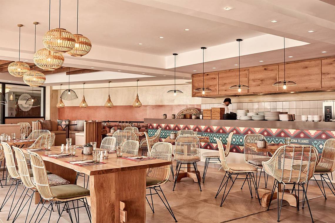 Innenansicht des Restaurants im Atlantica Caldera Palace Hotel mit Holztischen, Rattanstühlen und dekorativen Wandmustern.