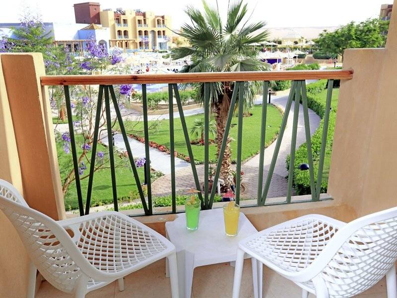 Ein Balkon mit Blick auf ein Hotel und einen Pool, zwei weiße Stühle und ein Tisch mit Getränken.