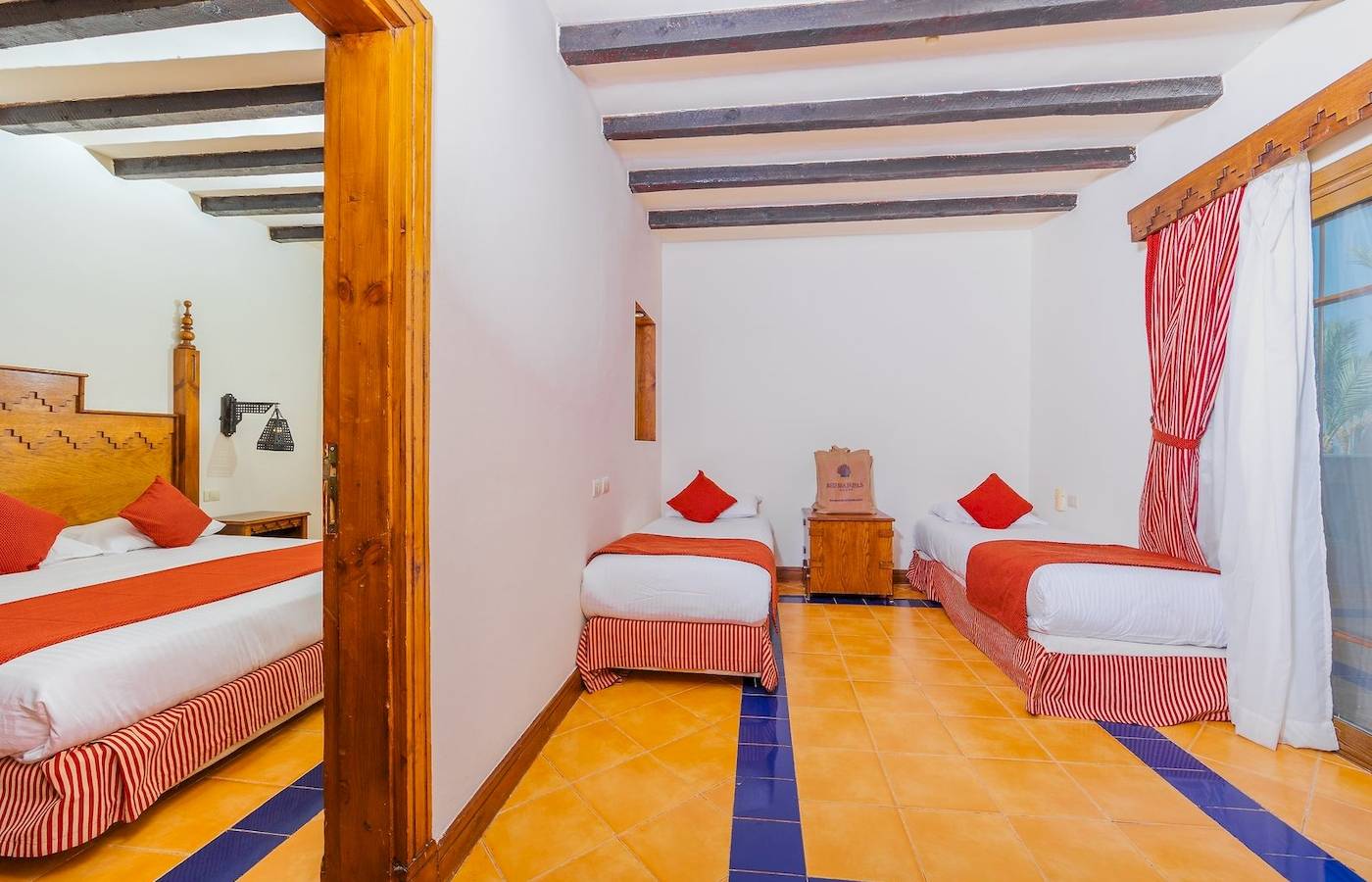 Dreibettzimmer im Grand Makadi Hotel mit blauen und gelben Fliesen und drei Betten.