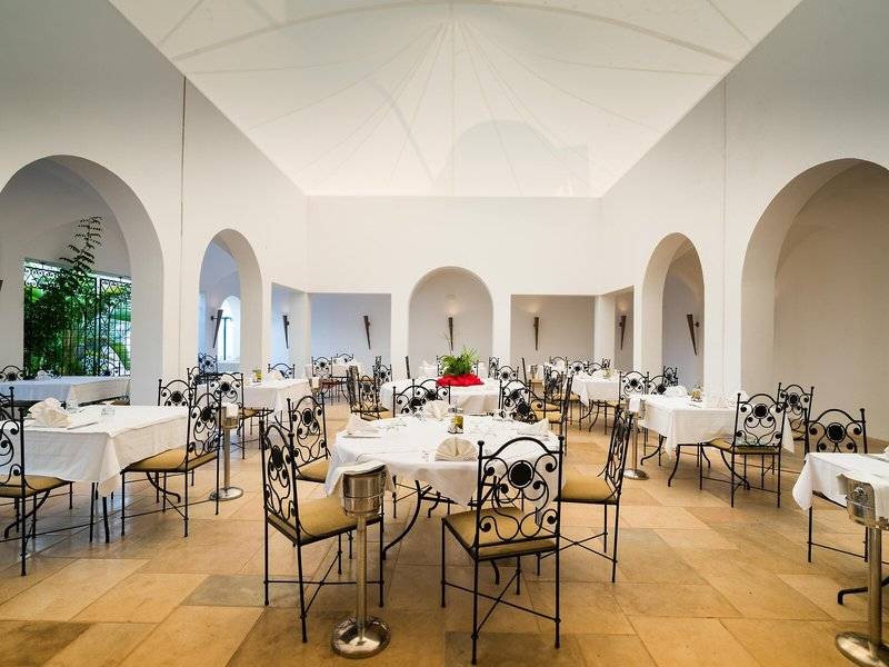 Restaurantsaal im Hotel Iliade Djerba by Magic Hotels mit weißen Tischen und Stühlen.