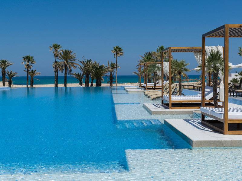 Außenpool des JAZ Tour Khalef Hotels mit Palmen und Blick auf den Strand