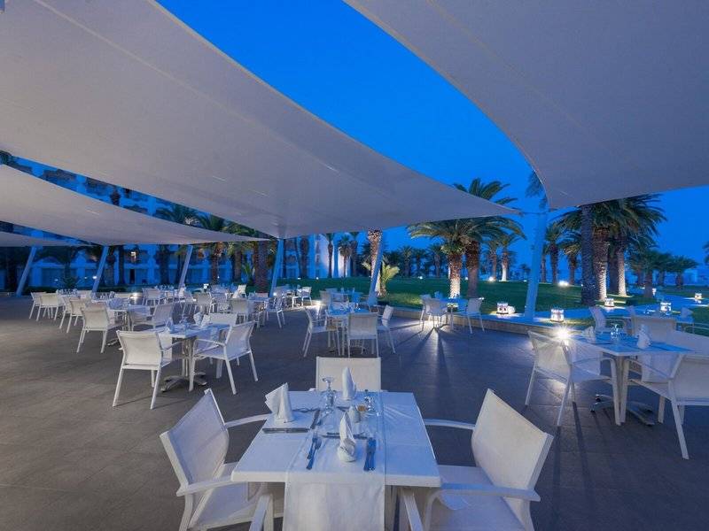 Außenbereich des JAZ Tour Khalef Hotels am Abend mit vielen weißen Tischen und Stühlen unter großen Markisen.