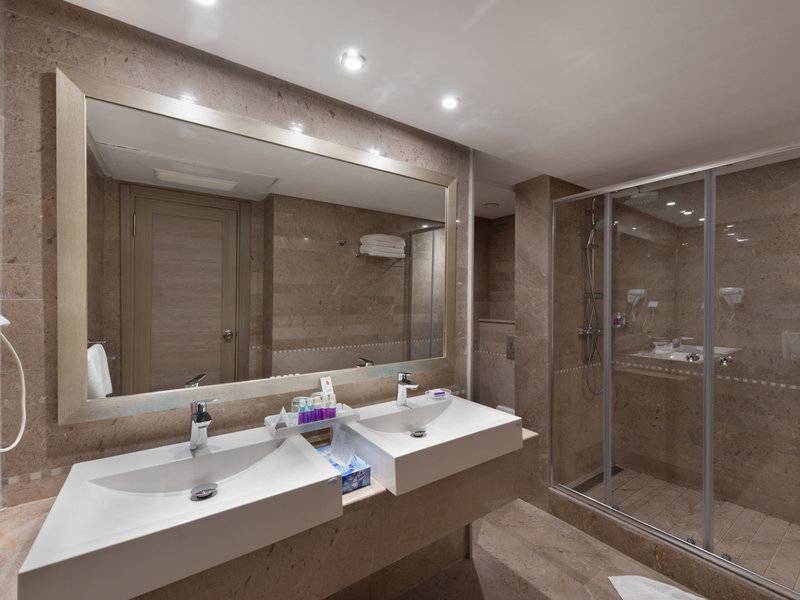 Badezimmer mit zwei Waschbecken, einem großen Spiegel und einer Glasdusche im JAZ Tour Khalef Hotel