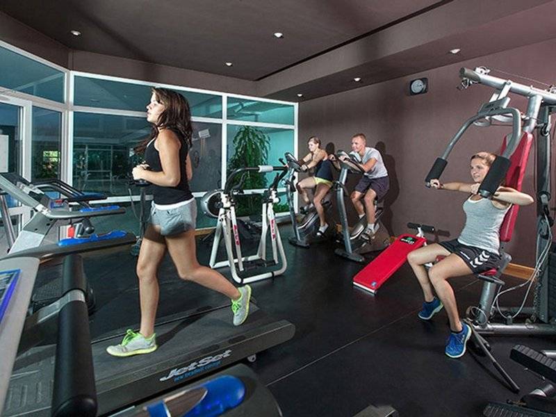 Fitnessstudio im Sahara Beach AquaPark Resort mit mehreren Personen, die auf Laufbändern und anderen Geräten trainieren.