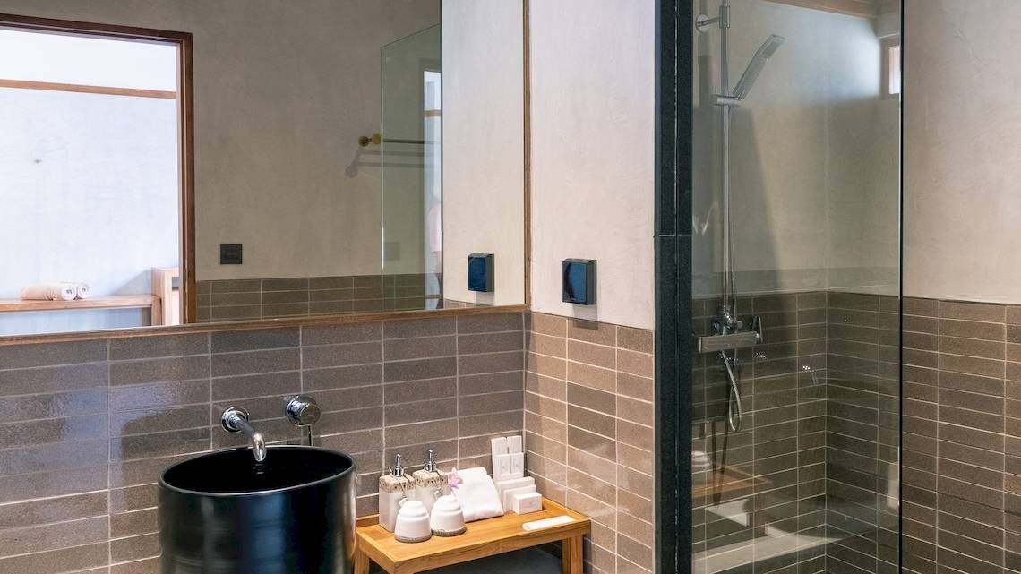 Badezimmer im Banana Fan Sea Resort mit schwarzen Waschbecken, Glasdusche und gefliester Wand.