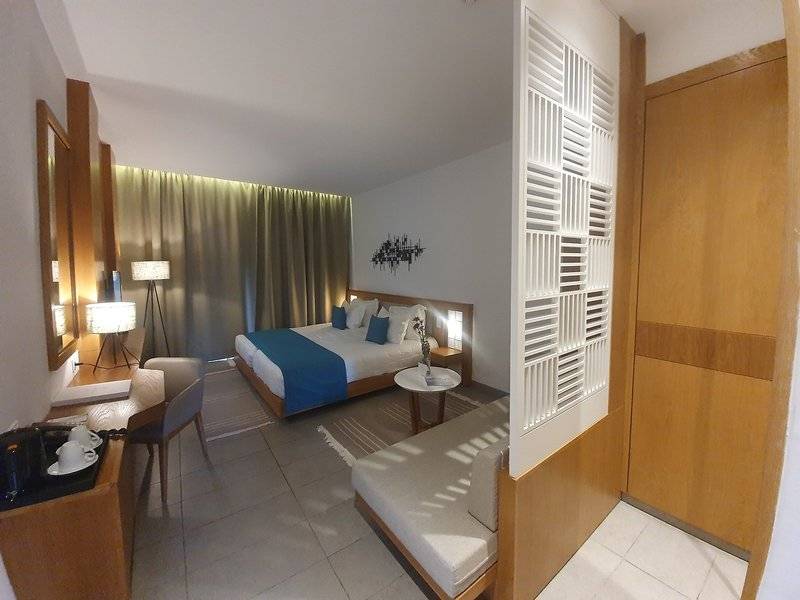 Innenansicht eines Hotelzimmers in den Orangers Garden Villas & Bungalows mit Bett, Sofa, Schreibtisch und Dekor.