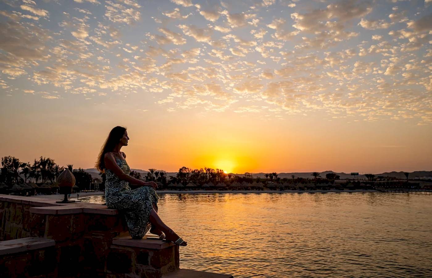 Eine Frau sitzt am Wasser während des Sonnenuntergangs im Mövenpick Resort El Quseir.