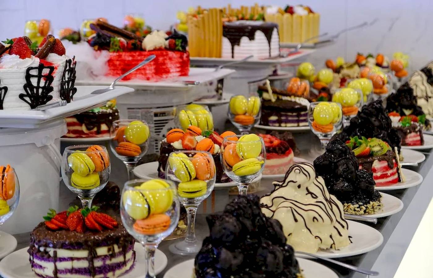 Club Wasa Holiday Village Kuchenbuffet mit verschiedenen Kuchen und Macarons auf weißen Tellern.