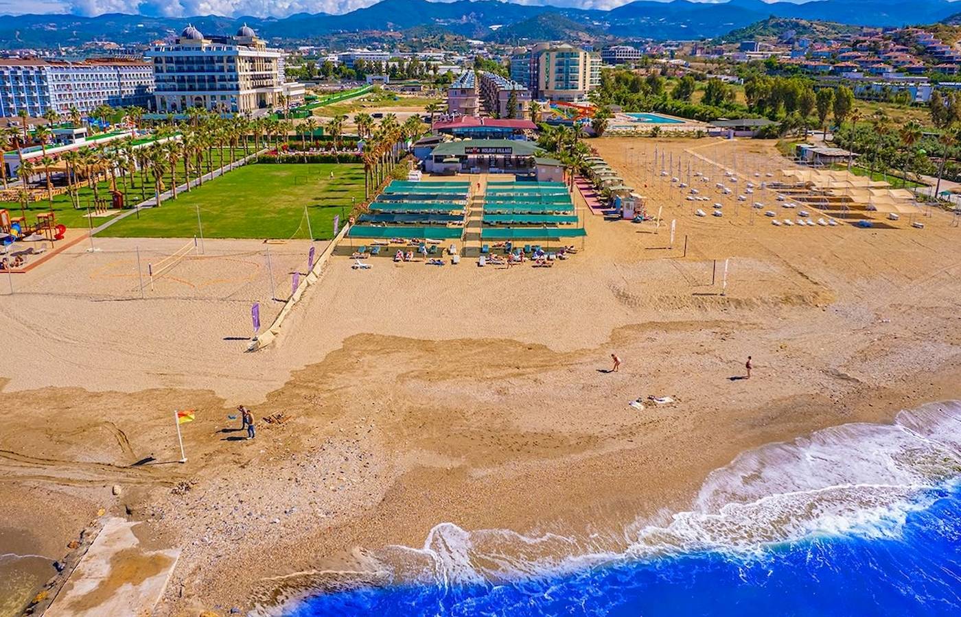 Luftaufnahme des Club Wasa Holiday Village Strands mit Hotels, Palmen und Wellen