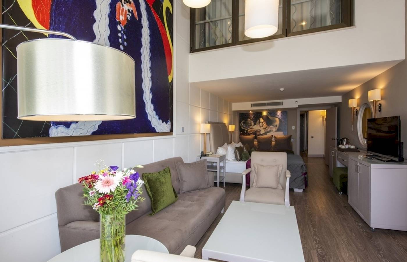 Innenraum der Suite im Side Star Elegance Hotel mit Wohnzimmer, Couch, Tisch, Sessel, Fernseher und Kunstwerk.