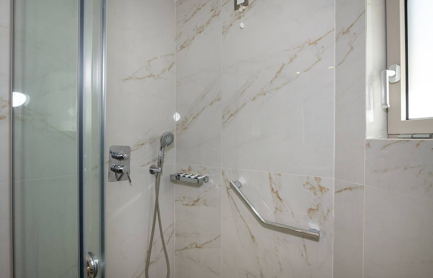 Eine Dusche mit marmorierten Wänden und Edelstahlgriffen im Vantari Luxury Beach Resort.