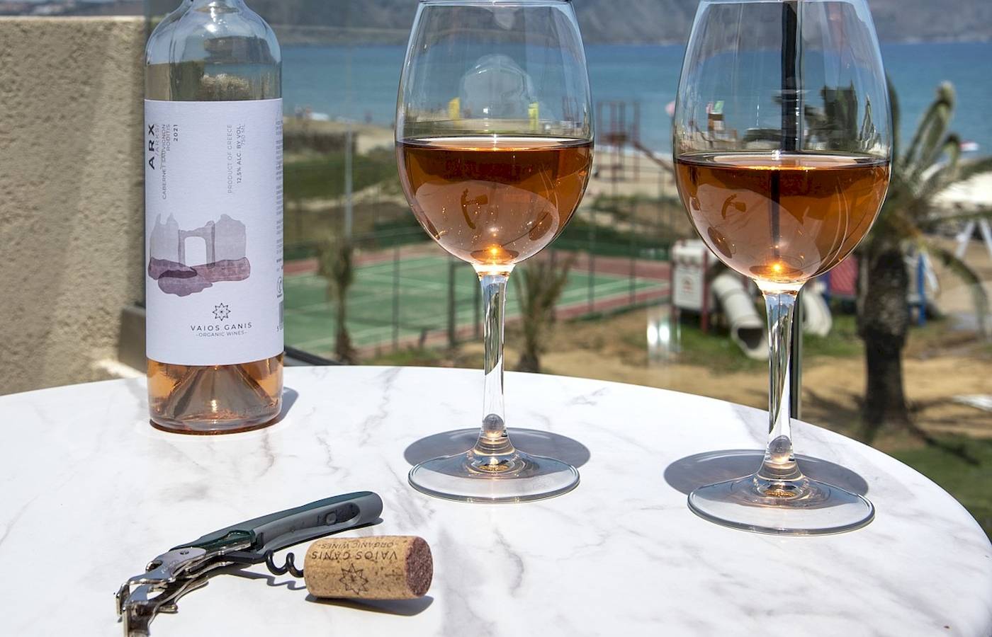 Eine Flasche Wein, zwei Gläser und ein Korkenzieher auf einem Tisch am Strand.