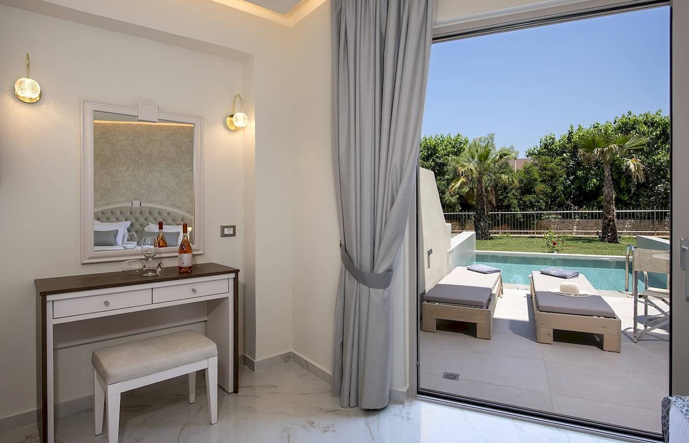 Innenansicht eines Zimmers im Vantaris Luxury Beach Resort mit Blick auf einen Swimmingpool und Liegen.