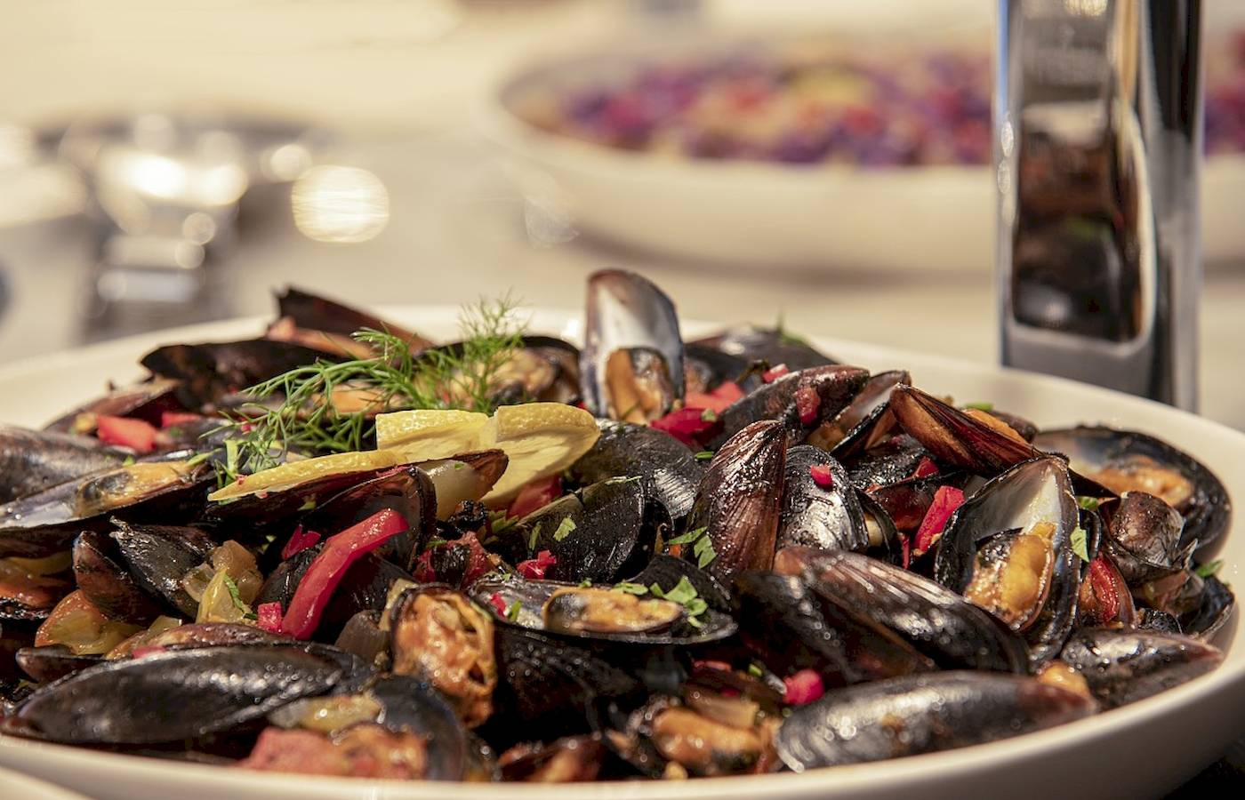 Eine Schüssel mit Muscheln, Paprika, Zwiebeln und Kräutern auf einem Tisch.