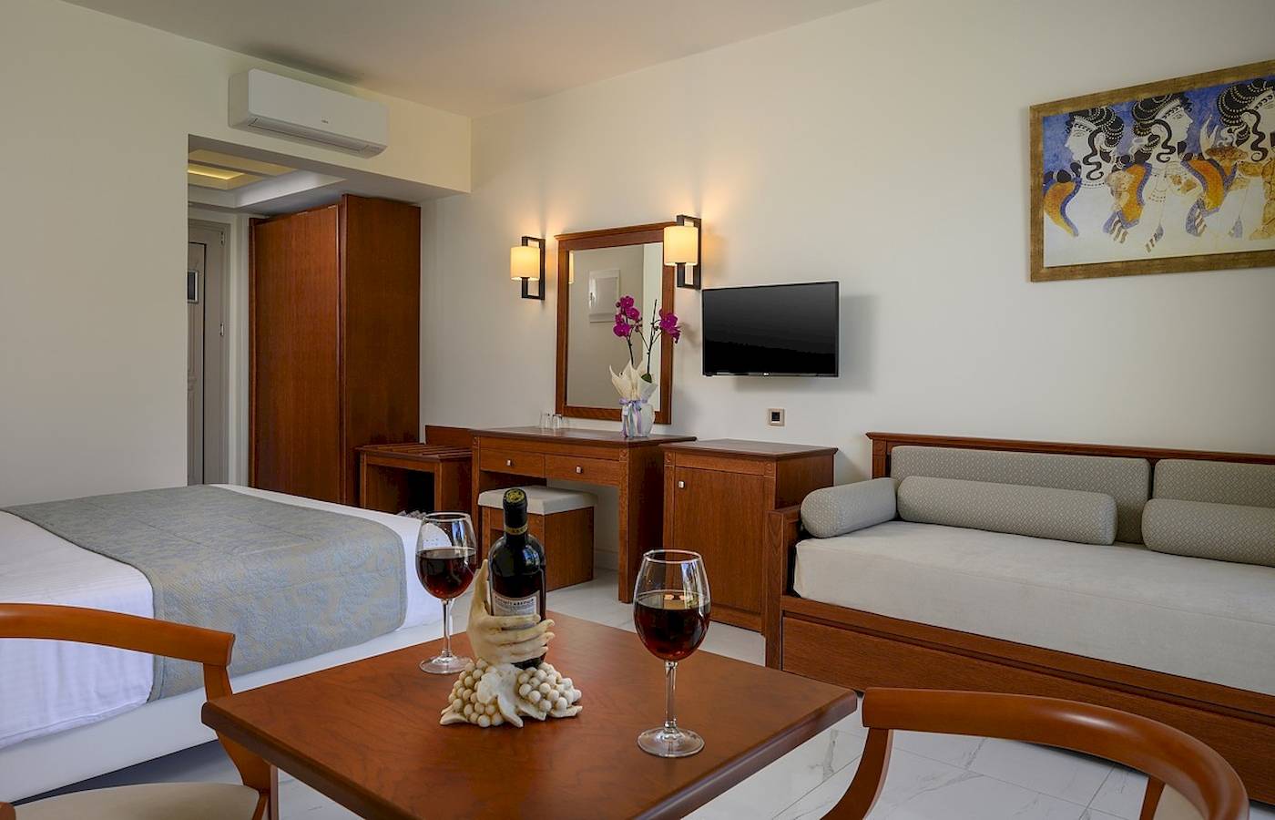 Innenansicht eines Zimmers im Vantaris Palace Hotel mit Bett, Tisch, Wein und Dekor.
