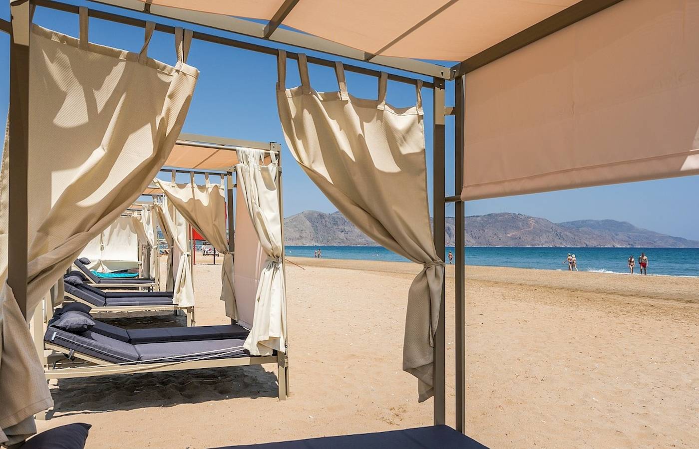 Sonnenliegen am Strand unter Pavillons am Vantaris Palace Hotel