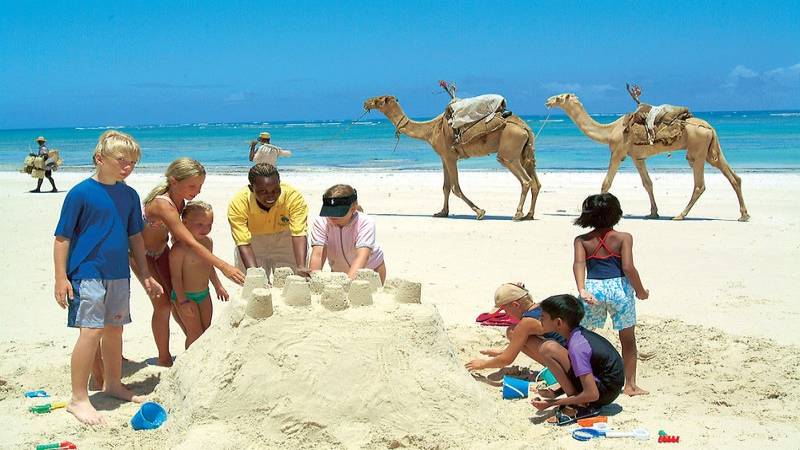 Kinder bauen einen Sandburg am Strand des Southern Palms Beach Resorts mit Kamelen im Hintergrund.