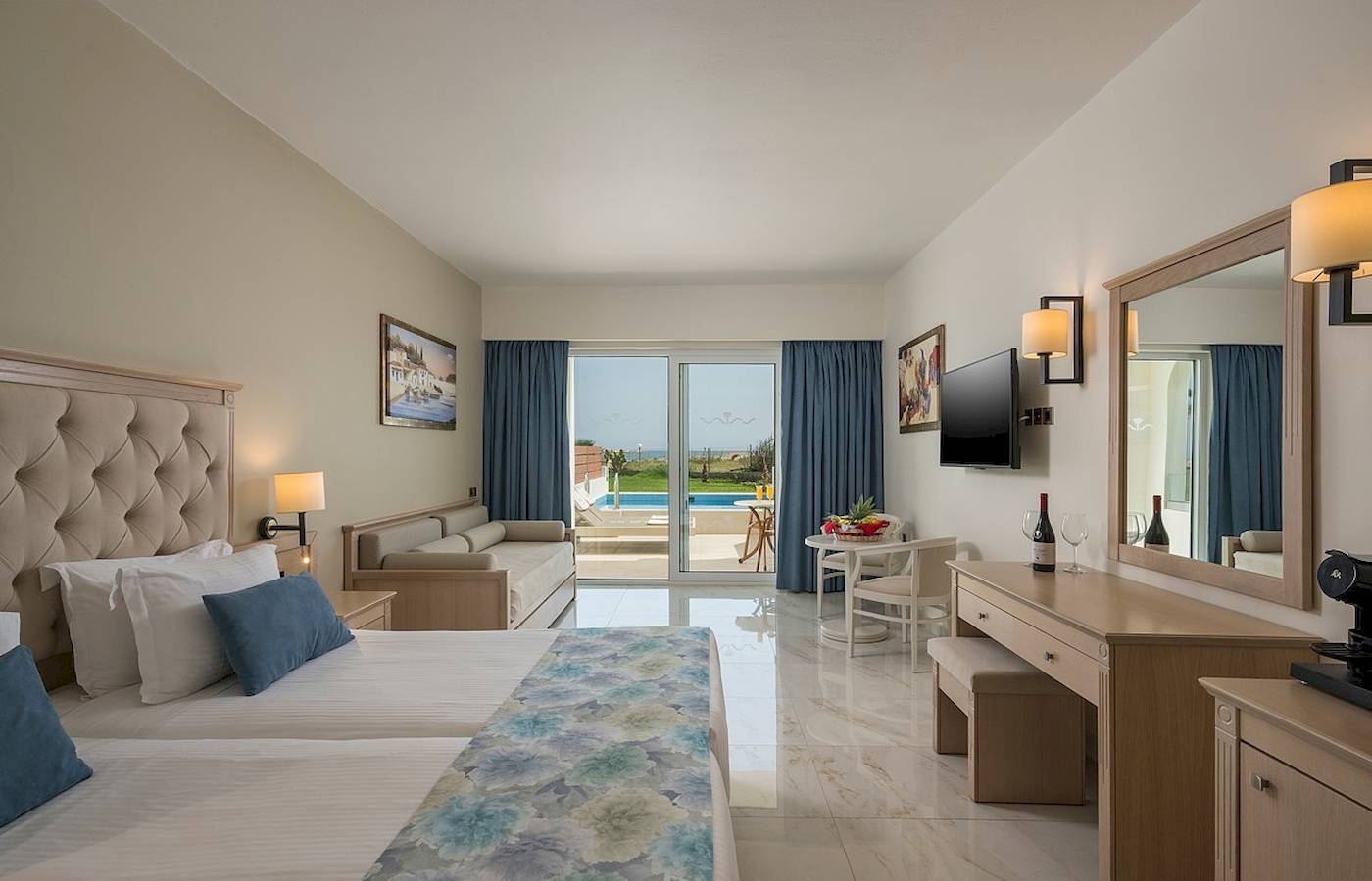 Hotelzimmer im Vantaris Palace mit zwei Betten, Sofa und großem Fenster, das zum Poolbereich führt.
