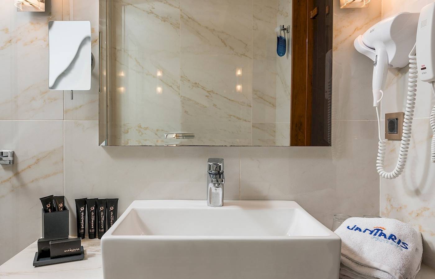 Badezimmer im Vantaris Palace Hotel mit Waschbecken, Spiegel und Handtuchtrockner.