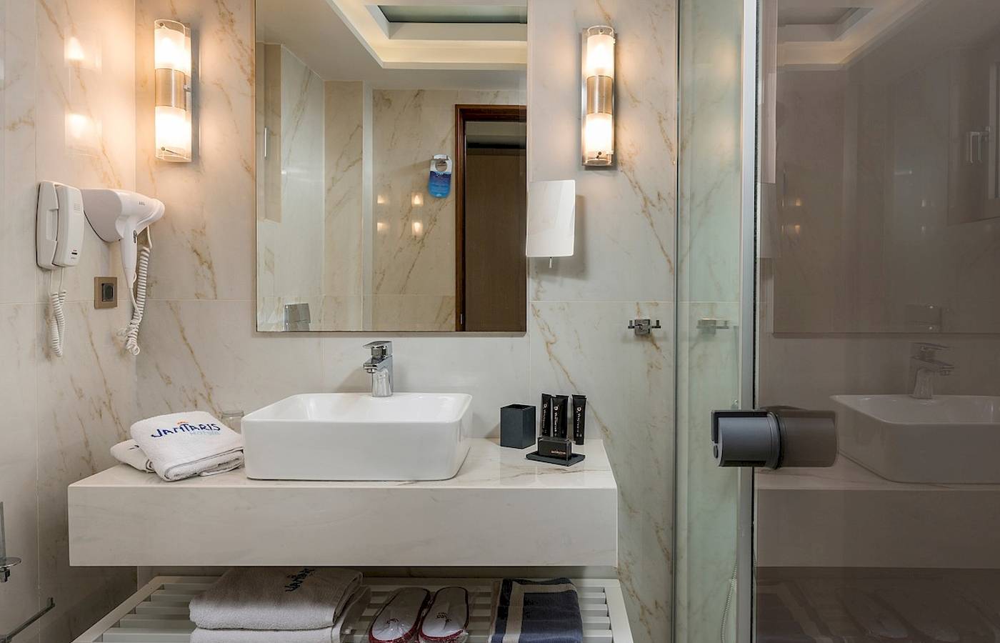Badezimmer im Vantaris Palace Hotel mit Waschbecken, Handtüchern und Toilettenartikeln.