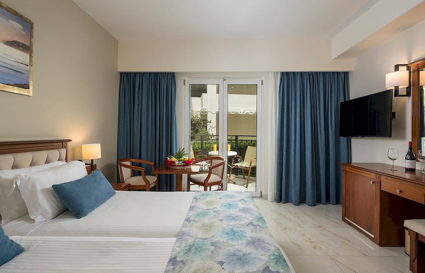 Innenansicht eines Schlafzimmers im Vantaris Palace Hotel mit zwei Betten, Tisch, Stühlen und Balkon.