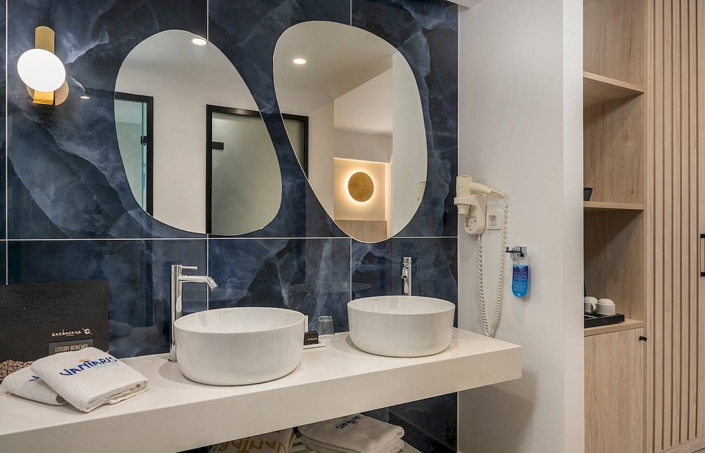Badezimmer im Vantaris Palace mit zwei Waschbecken, Spiegeln und blauer Wandgestaltung.