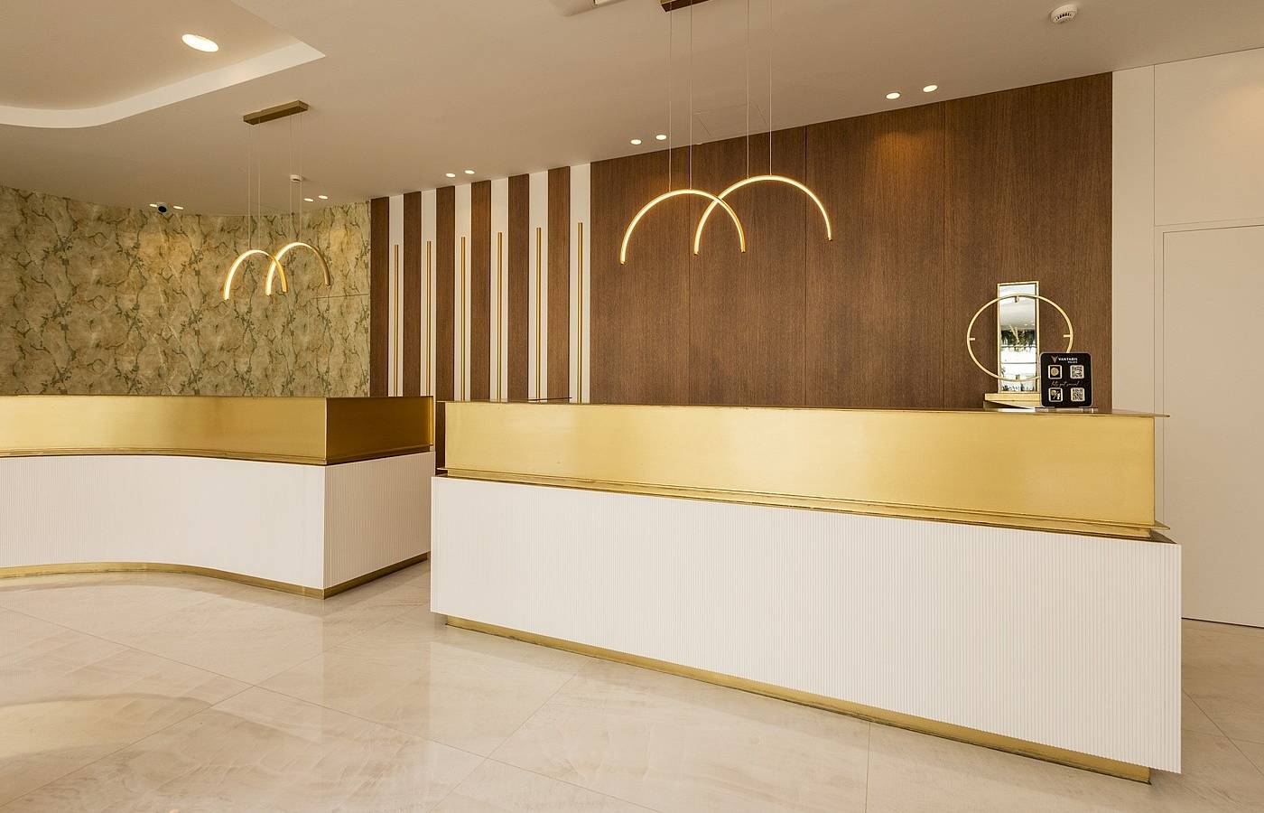 Empfangsbereich des Vantaris Palace Hotels mit goldfarbener Theke und dekorativen Kronleuchtern.