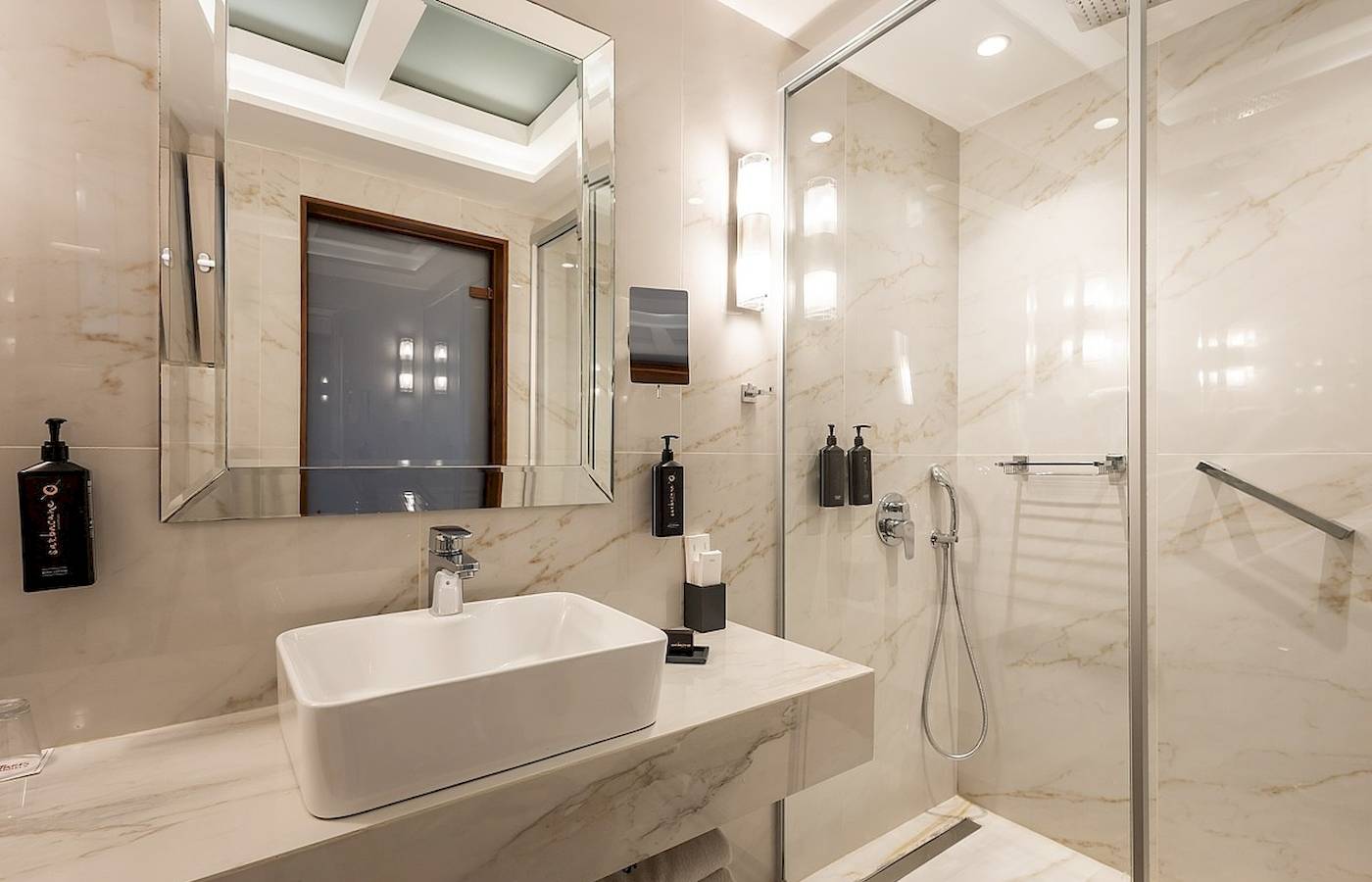 Badezimmer im Vantaris Palace mit Marmorfliesen, Dusche und Waschbecken.