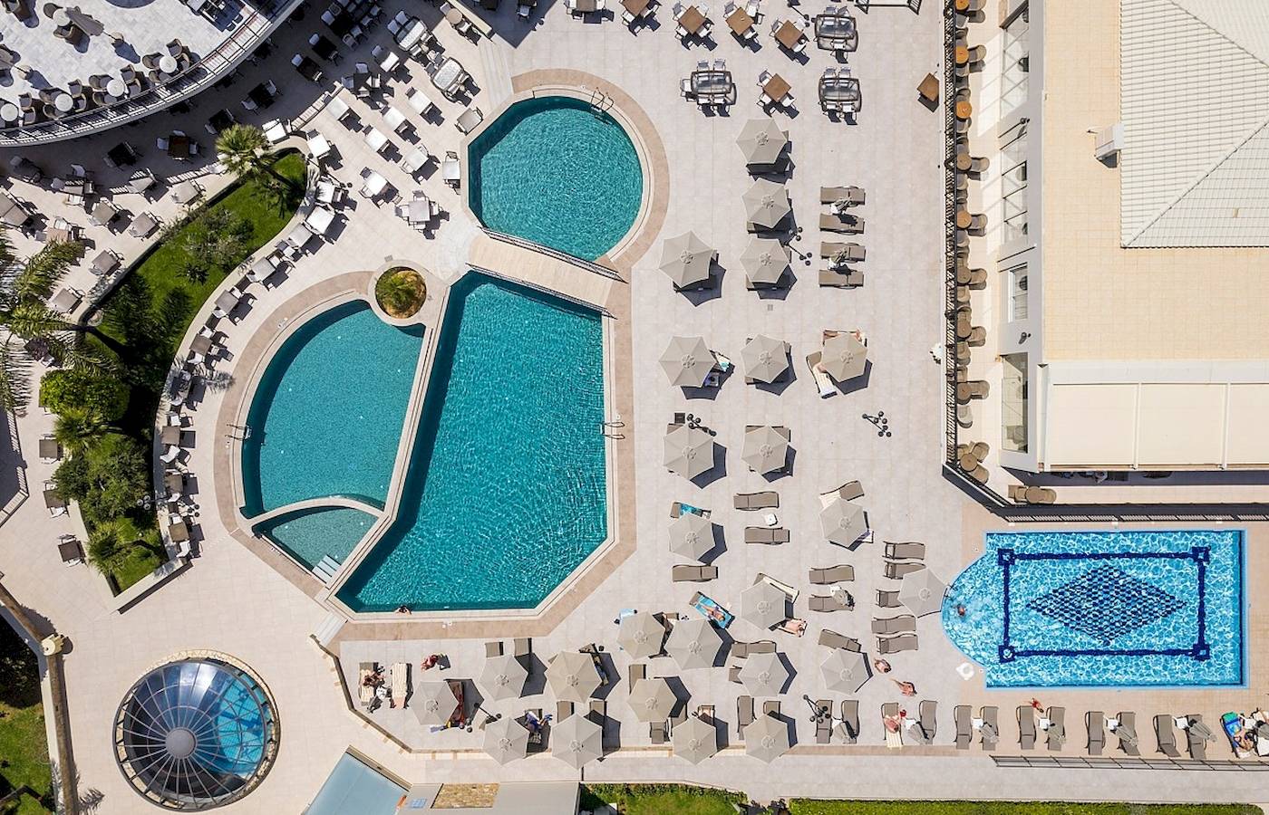Luftaufnahme des Vantaris Palace Schwimmbadbereichs mit mehreren Pools und Sonnenliegen.