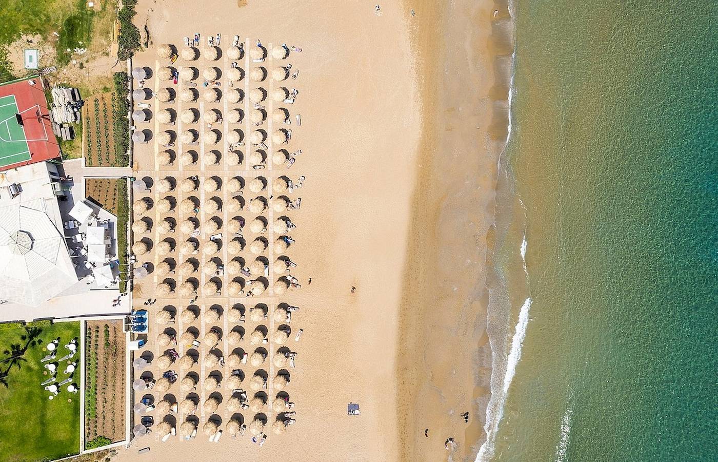 Oberflächenansicht eines Strandes mit vielen Sonnenhüten und einem Hotelgebäude im Hintergrund.