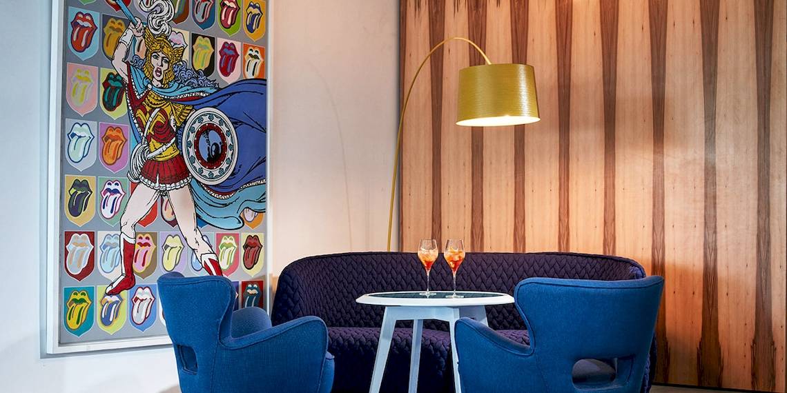 Innenbereich des Myconian Ambassador Hotels mit einem Sofa, einem Tisch und einer Wand mit Rolling Stones Kunstwerk.