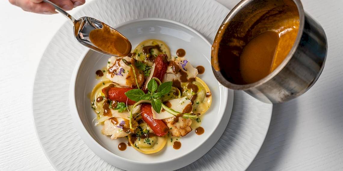 Ein Tellergericht mit gefüllten Teigtaschen, Tomaten, Basilikum und einer braunen Sauce.