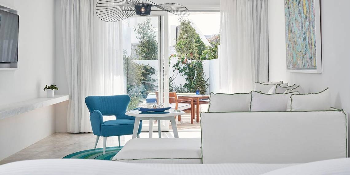 Innenansicht der Myconian Ambassador Relais & Chateaux Suite mit weißem Interieur, blauem Stuhl, weißem Tisch und Wohnzimmermöbeln.