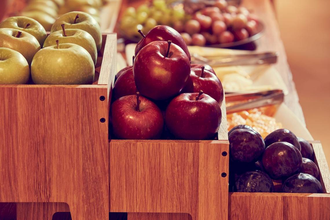 Holzboxen mit verschiedenen Obstsorten wie roten Äpfeln, grünen Äpfeln und Pflaumen.