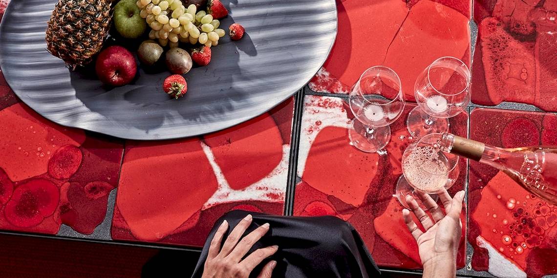 Frühstück im Bett im Myconian Ambassador Relais & Chateaux mit Früchten und Sekt auf rotem Tisch