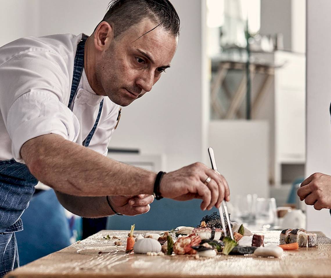Koch im Myconian Ambassador Relais & Chateaux, der Sushi auf einem Holztisch zubereitet.