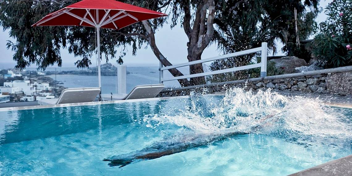 Ein Pool mit einer roten Sonnenschirm und Blick auf eine Stadt und Meer.