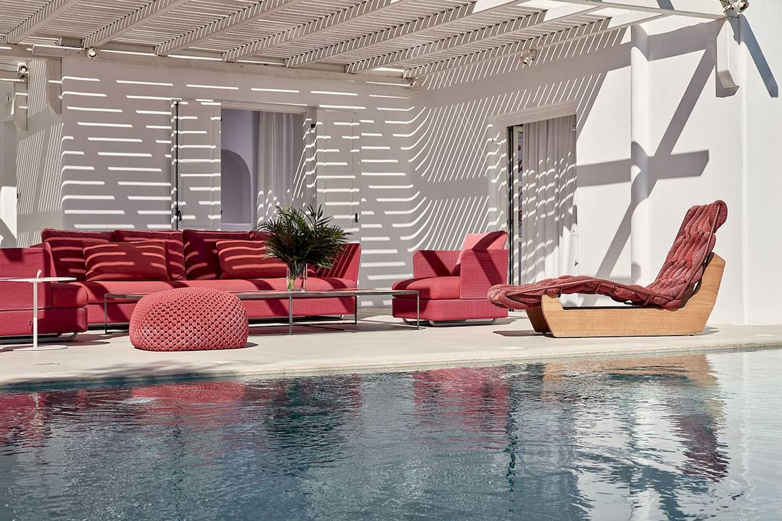 Poollounge im Myconian Ambassador Hotel mit roten Möbeln und einem weißen Gebäude.