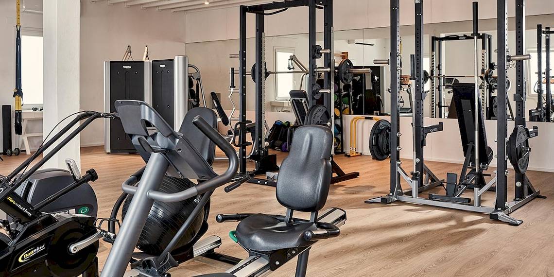 Fitnessstudio im Myconian Ambassador Relais & Chateaux mit verschiedenen Trainingsgeräten und Holzboden.