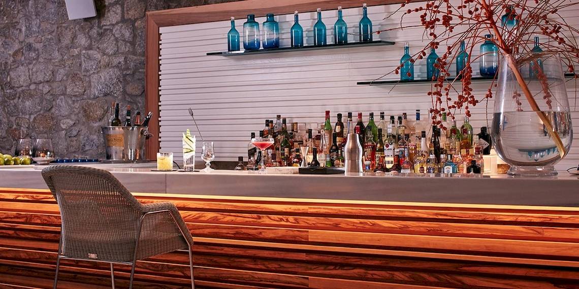 Bar-Theke im Myconian Ambassador Relais & Chateaux Hotel mit vielen Flaschen und Gläsern.