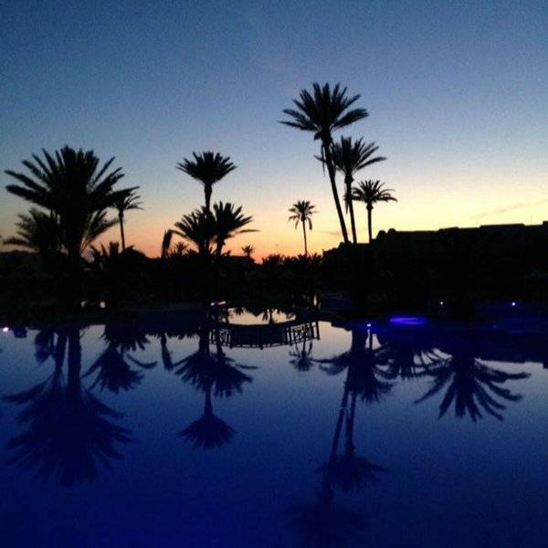Palmen um einen Pool im Djerba Holiday Beach Hotel bei Sonnenuntergang.
