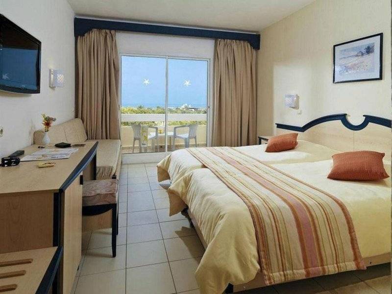 Zimmer im Djerba Holiday Beach Hotel mit zwei Betten, Balkon, Fernseher und Schreibtisch.