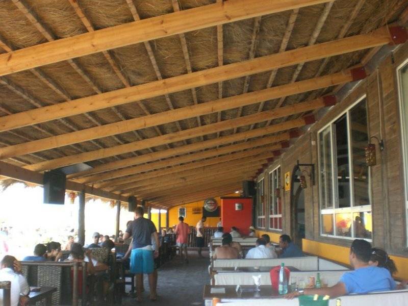 Innenansicht der Terrasse im Djerba Holiday Beach Hotel mit Gästen an Tischen und Holzbalkendecke.